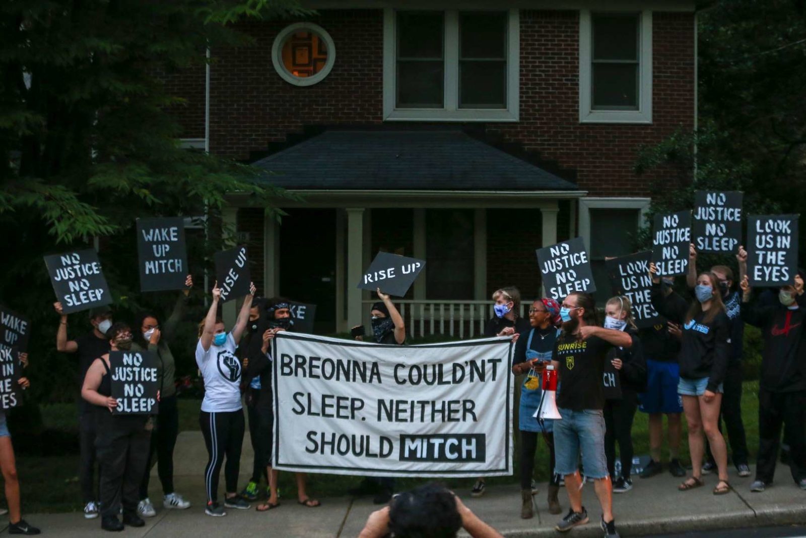Активисты восхода солнца проводят демонстрацию перед домом Митча Макконнелла в Кентукки, держа в руках большой плакат с надписью «Бреонна не могла спать. И Митч тоже не должен».
