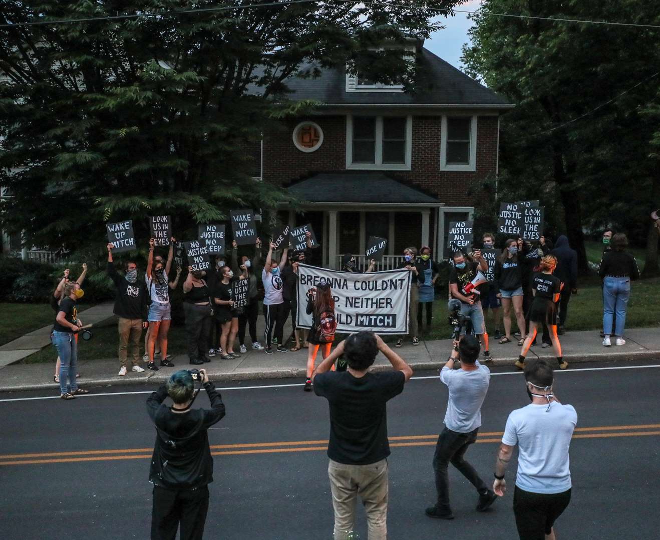 Sunrise activists fill the sidewalk in front of Mitch McConnell's KY house, holding a large sign saying "Breonna Couldn't Sleep. Neither Should Mitch".