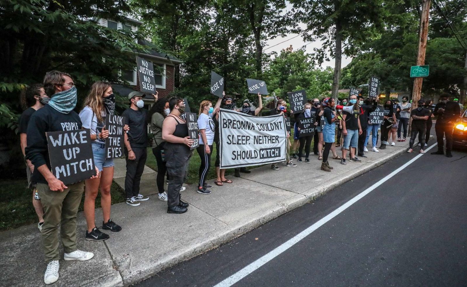 Ativistas do nascer do sol se alinham na calçada da casa KY de Mitch McConnell, segurando uma grande placa dizendo "Breonna não conseguia dormir. Mitch também não deveria".