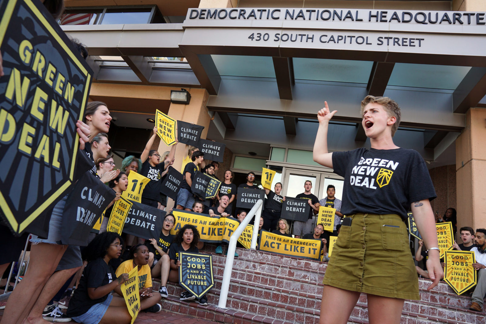 Un organizzatore di Sunrise guida un folto gruppo di compagni Sunrisers in una canzone mentre occupano l'ingresso del quartier generale del DNC a Washington.