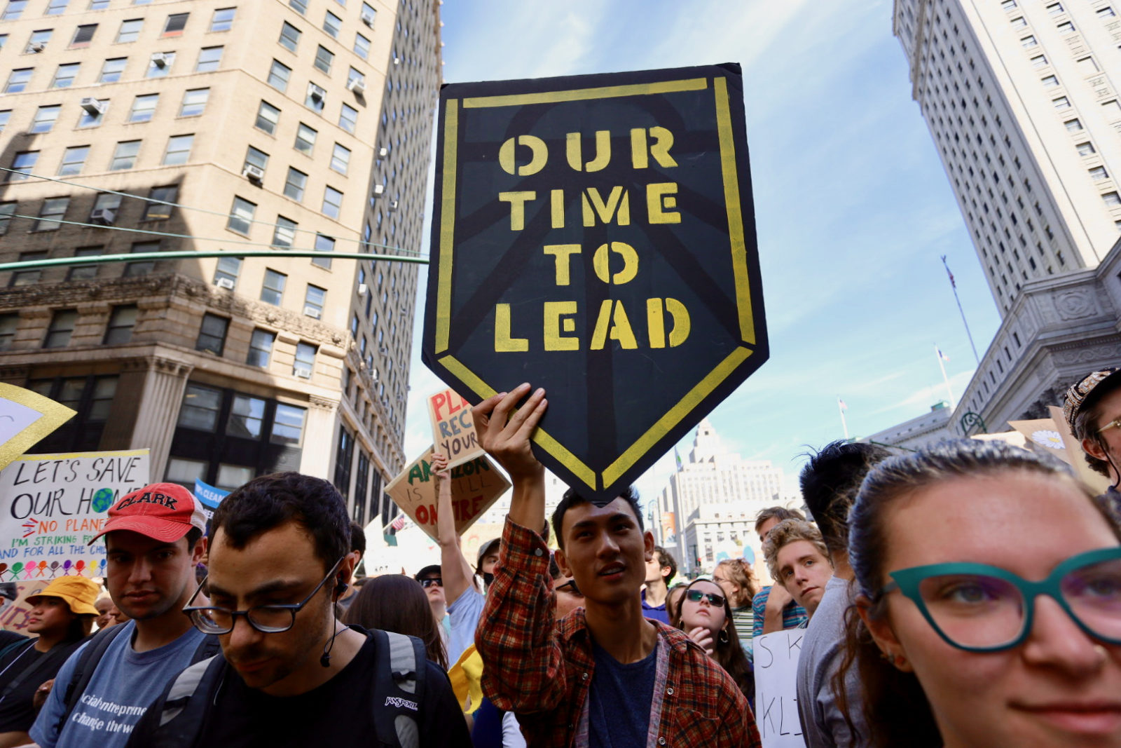 A crowd of protesters with one person holding a shield sign saying "Our time to lead".