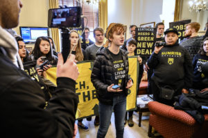 Young Sunrise Movement organizer speaks to cameras in front of crowd holding Green New Deal Banners. Photo by Ken Schles 5684