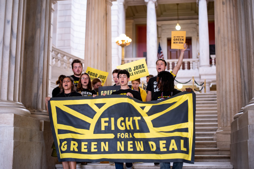a group of people in Sunrise shirts holding a banner reading "Fight for Green New Deal"
