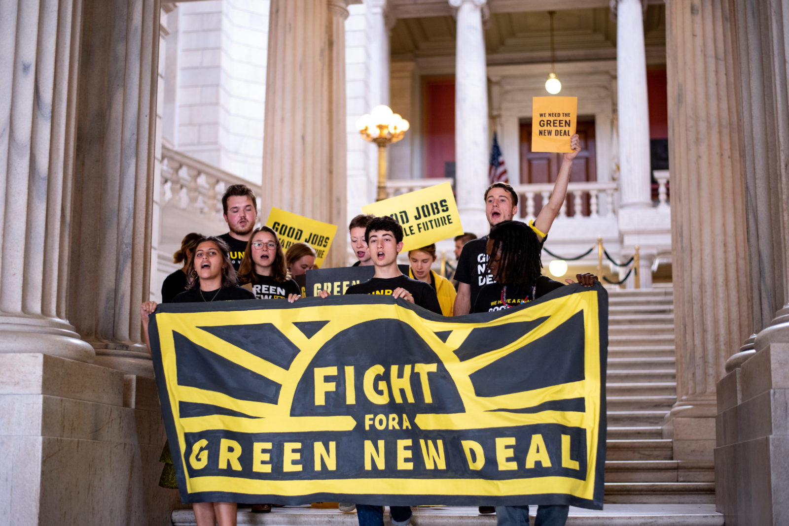 un gruppo di persone in magliette Sunrise con in mano uno striscione con la scritta "Fight for Green New Deal"