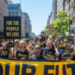 Sunrisers marching in the streets in DC with signs that read For the People We Love and For the Water We Drink