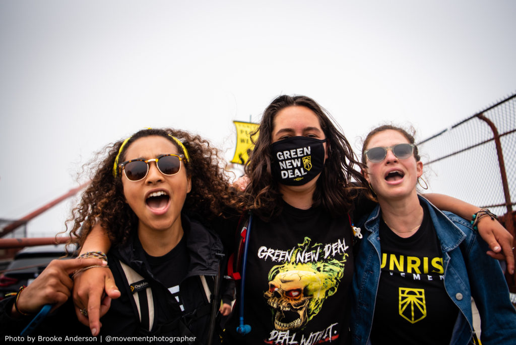 Três ativistas, de braço dado, marcham por um Green New Deal.